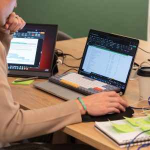 Person working on spreadsheets with laptops and notes.